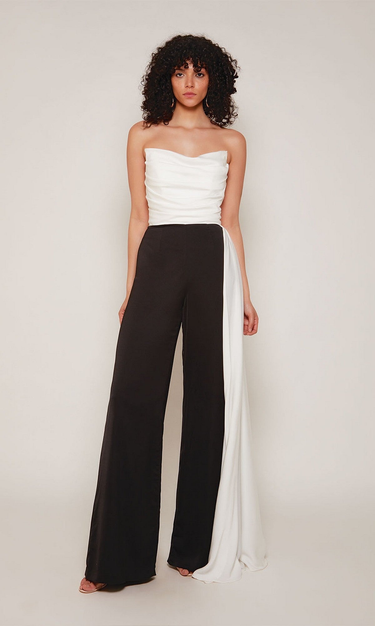 A woman poses against a plain background in the Alyce 70050 Long Formal Jumpsuit, featuring a strapless ruched white top, black wide-leg pants, and a sleek white side panel.